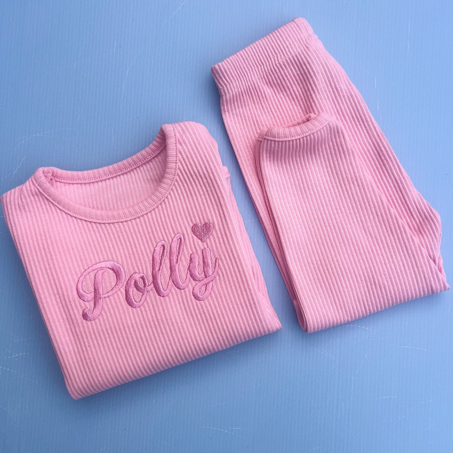 Pink ribbed pajama set with 'Polly' embroidery on a blue background