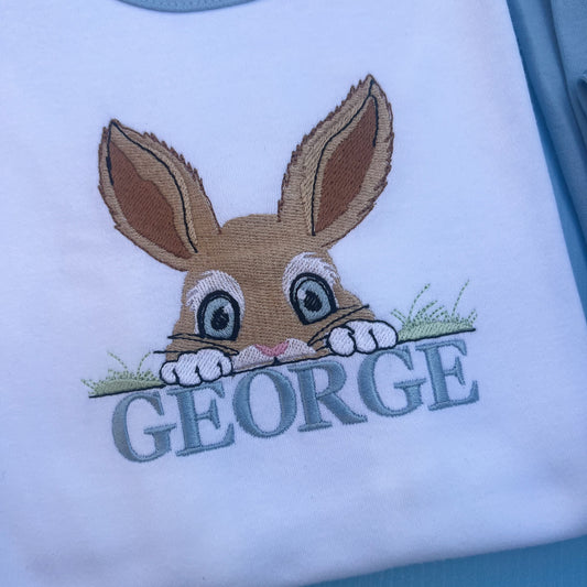 Blue pyjamas with a peaking bunny posting over grass embroidered on with the name George