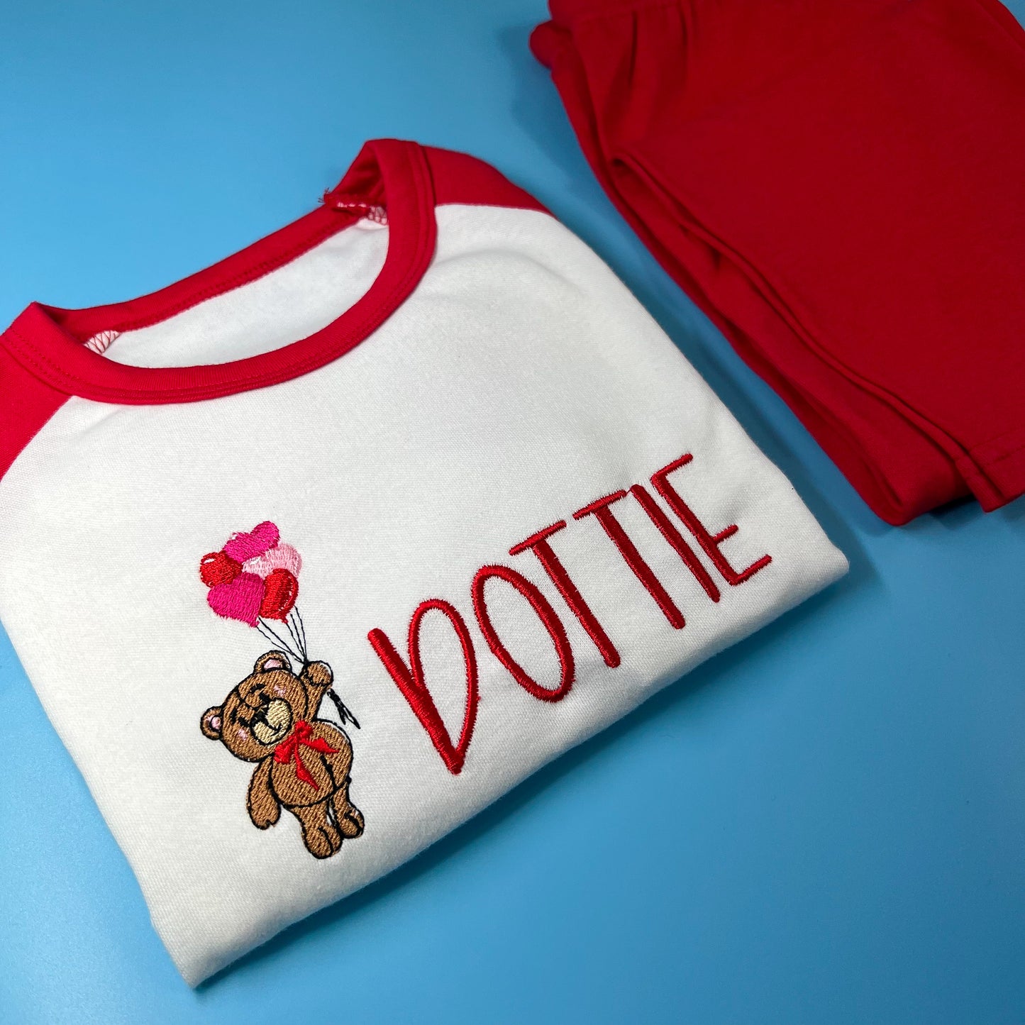 A set of children's pyjamas with a white top that has a red bear graphic and the name 'Dotty' written on it, and red pants with a small bear design.