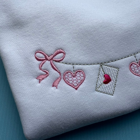 Embroidered heart and bow design on a light gray fabric background