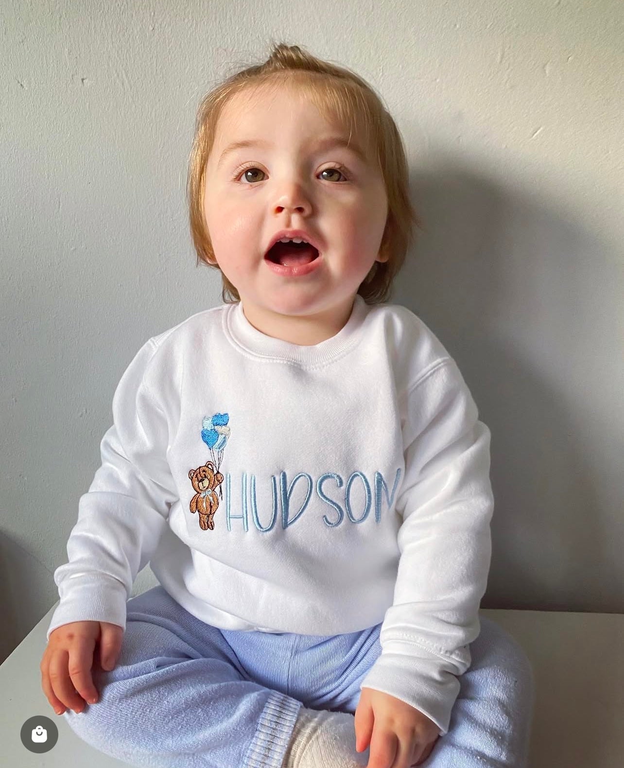 Boy wearing White jumper with teddy bear holding heart balloons embroidered on the front along with a name