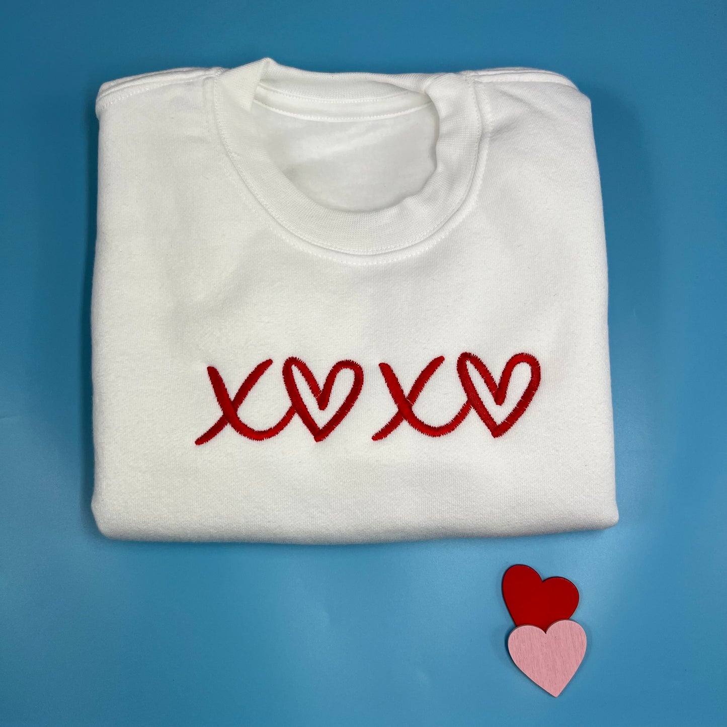 Folded white sweatshirt with red embroidered design on a blue background