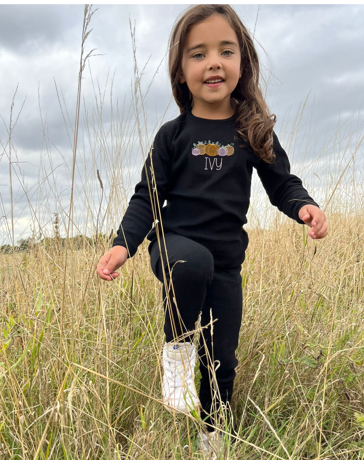young girl walking through field with black hallween tracksuit with pumpkins and her name embroidered