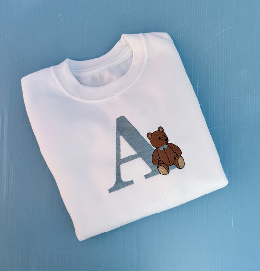 White sweatshirt with a teddy bear and letter 'A' on a blue background
