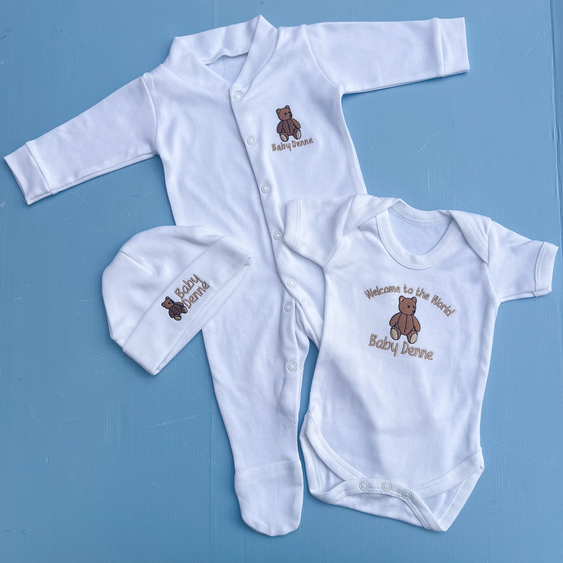 Baby clothing set with white romper, hat, and onesie on a blue background
