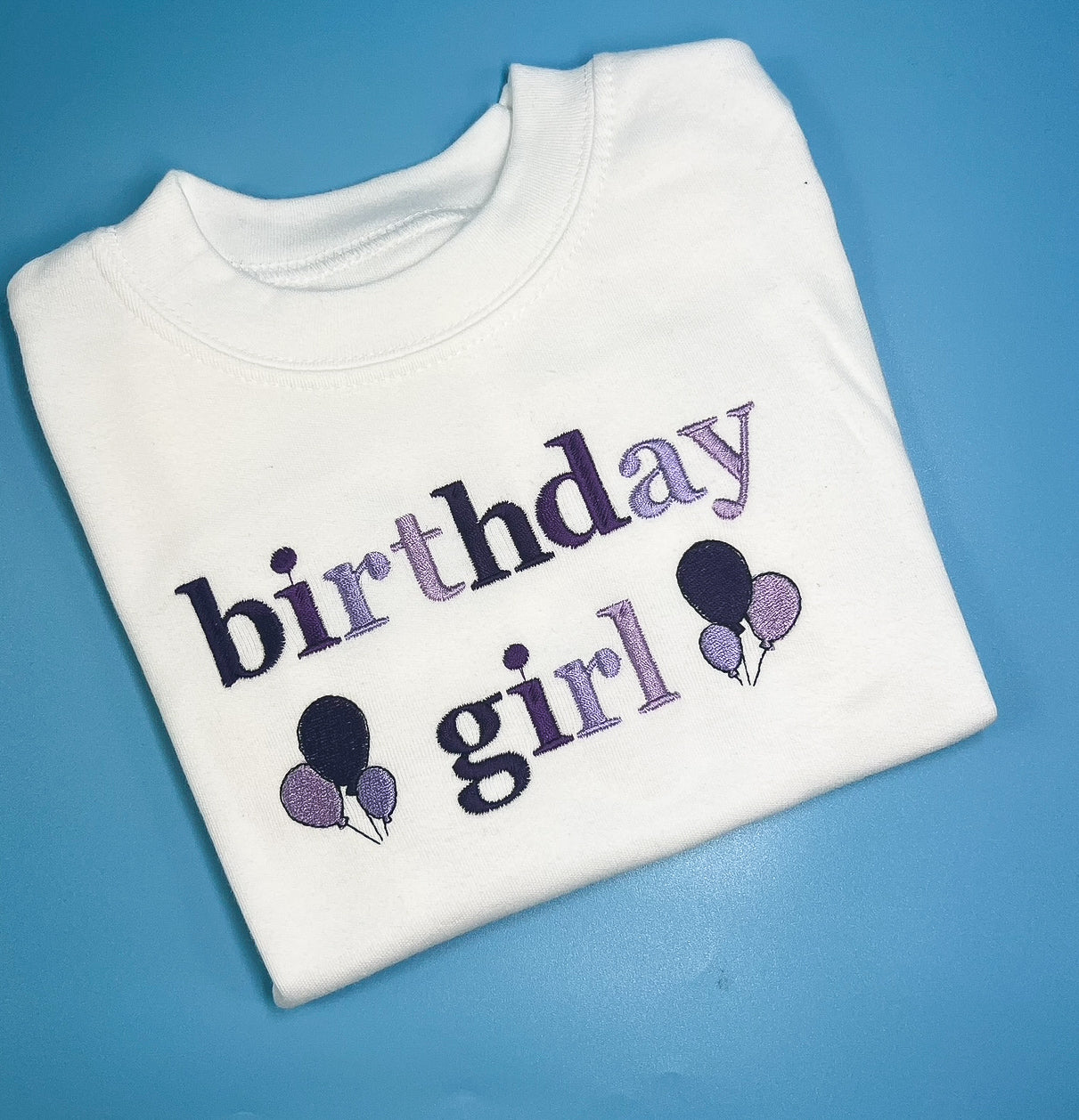 White sweatshirt with 'birthday girl' text and balloons on a blue background