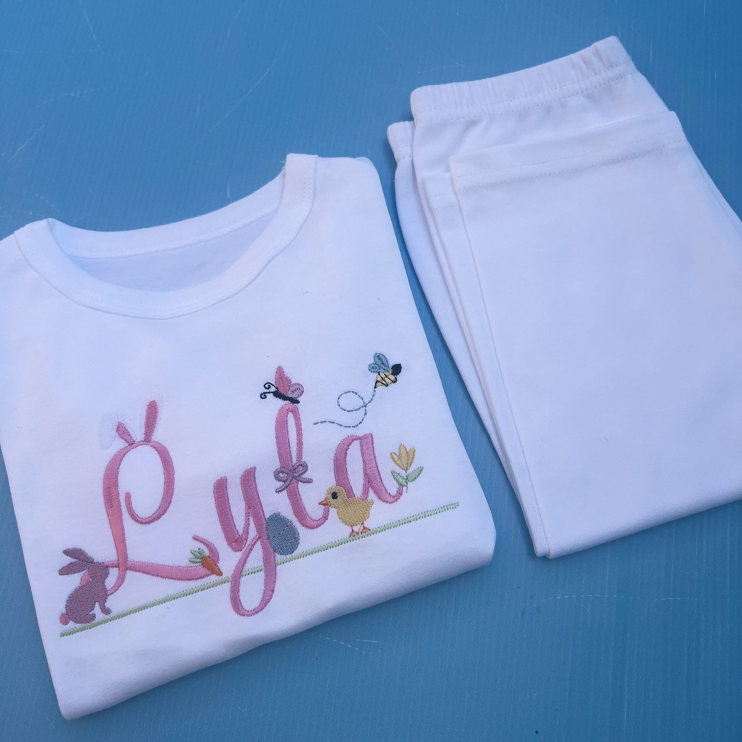 Name Lyla in pink with lots of Easter icons including, bunny rabbit ears, egg, bunny, chick, butter fly and bumble bee 