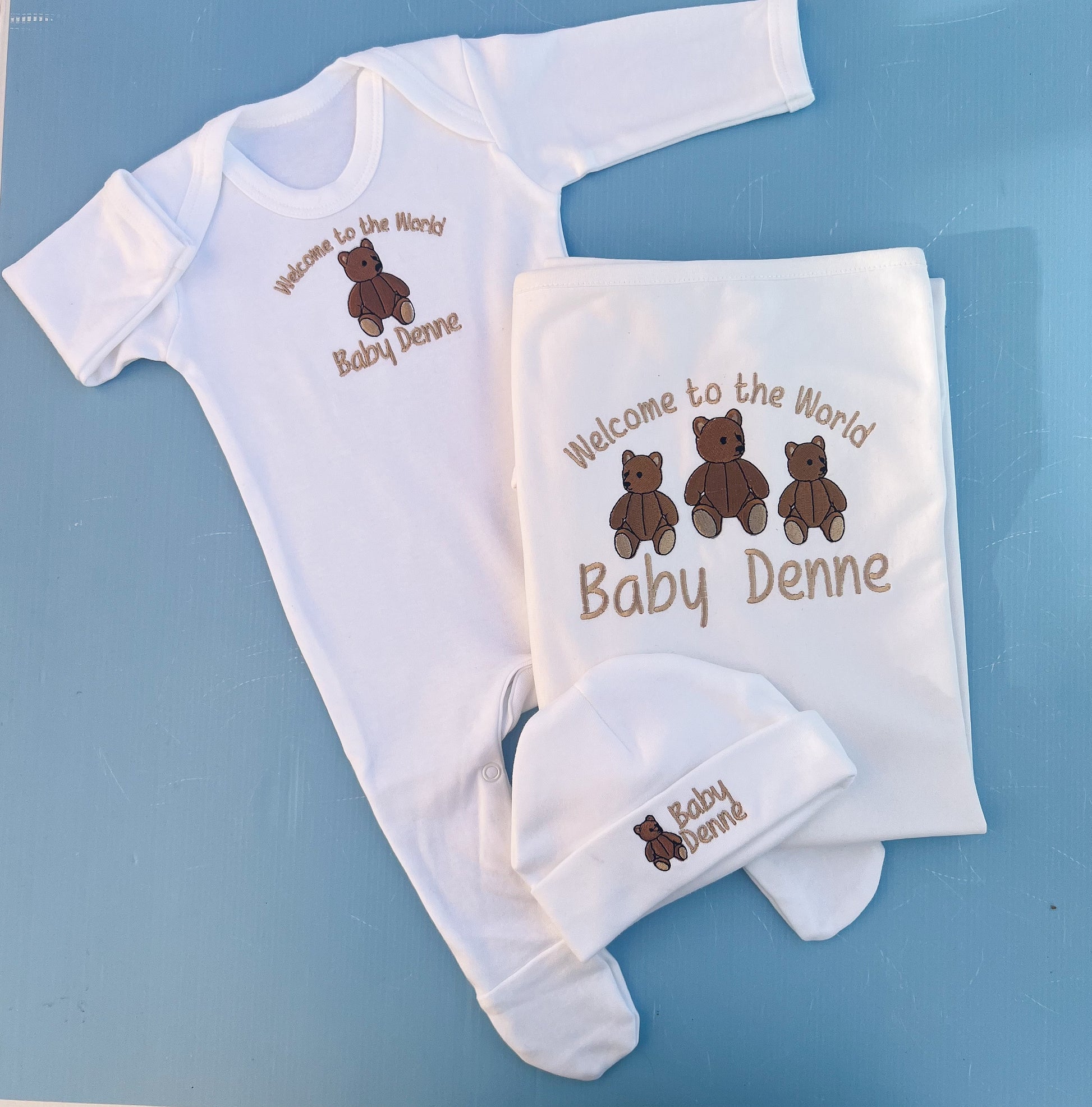 Baby clothing set with 'Welcome to the World Baby Denne' text on a blue background