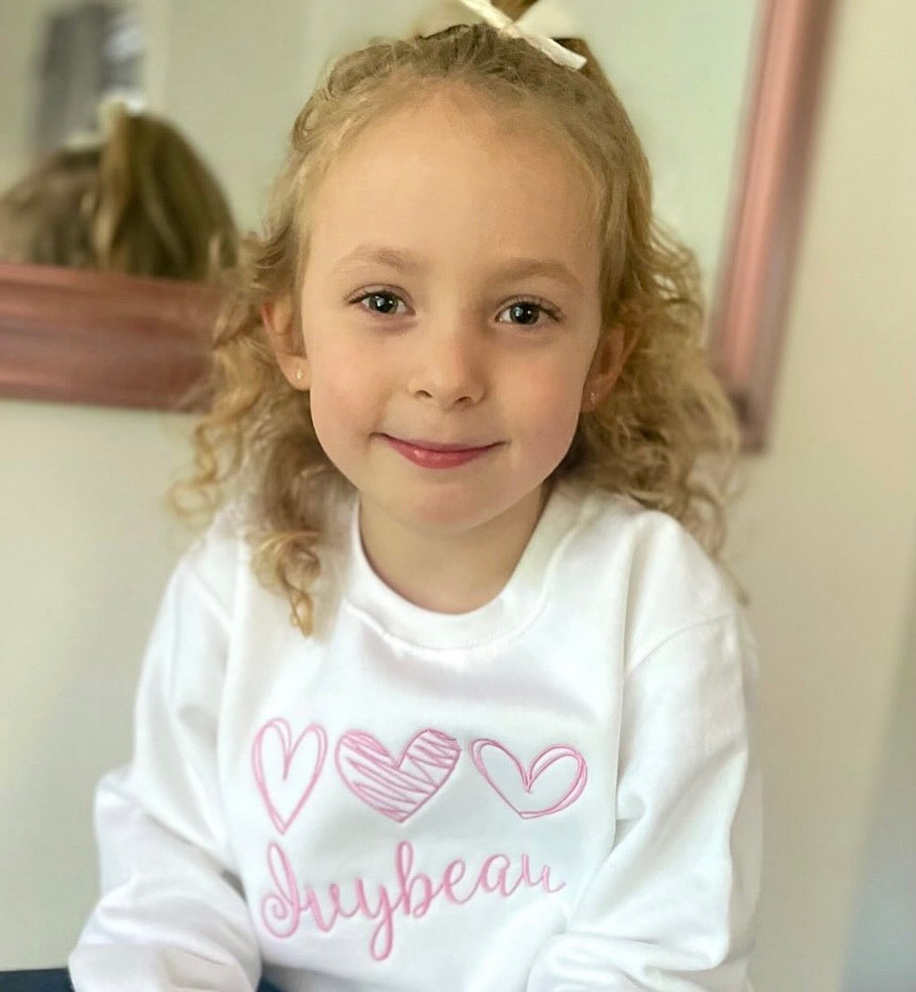 Girl wearing white jumper with pink embroidery 3 hearts 