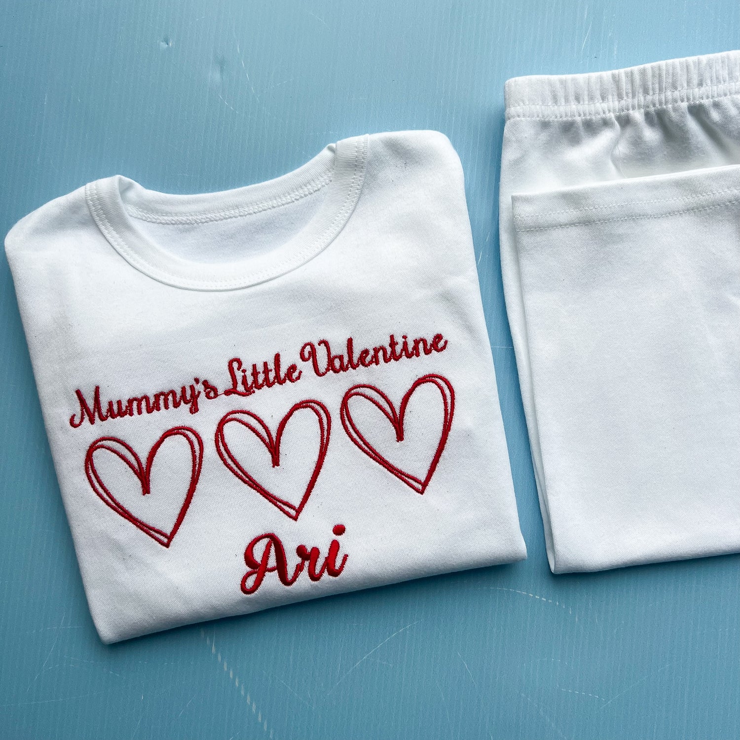 White pyjamas with red text and hearts on a blue surface