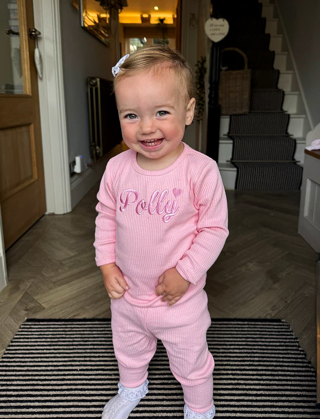 Child wearing a pink outfit with 'Polly' printed on it, standing indoors.
