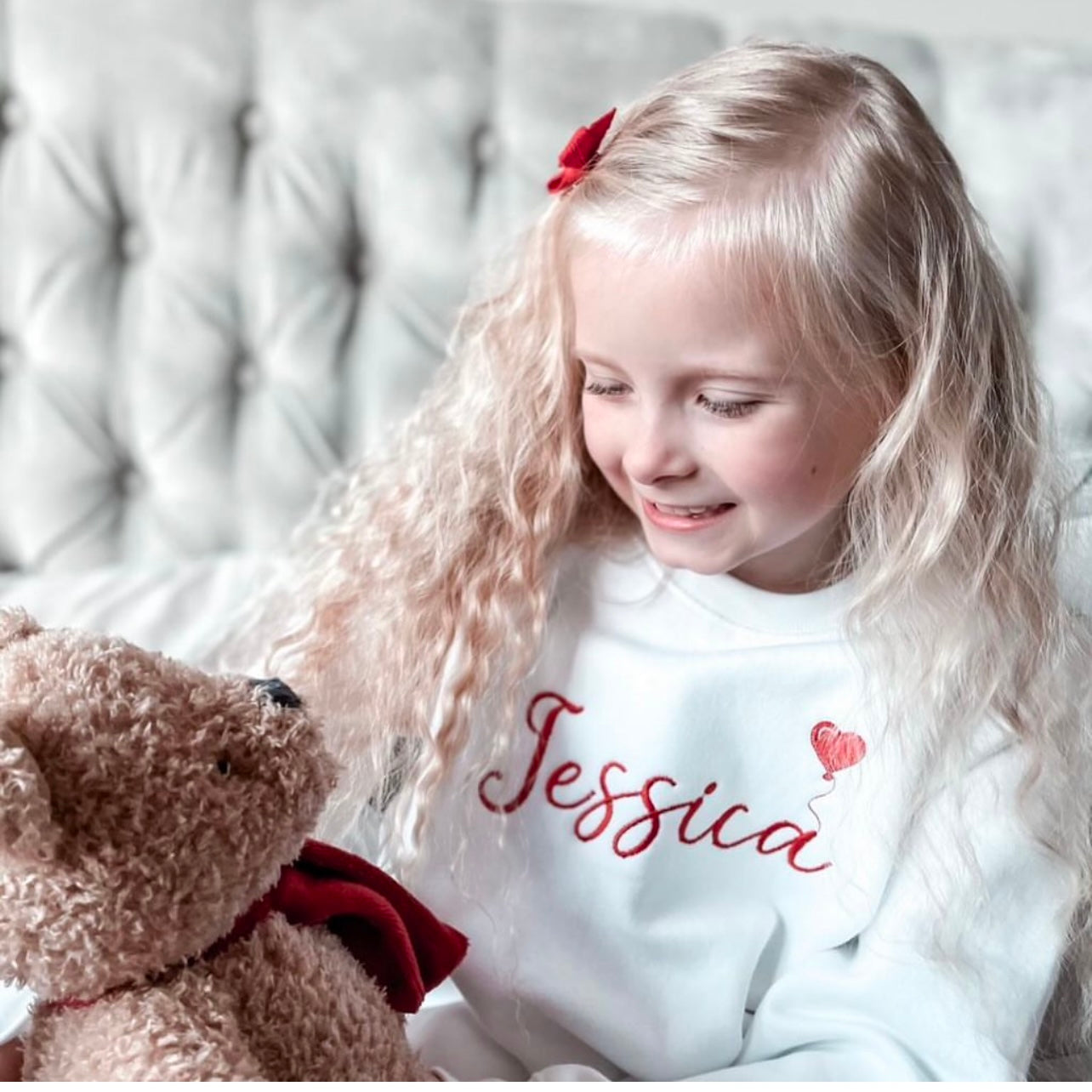 A girl wearing a white sweatshirt with Jessica and a red balloon on the front 