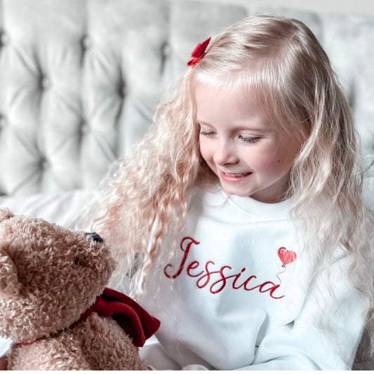 A girl wearing a white sweatshirt with Jessica and a red balloon on the front 