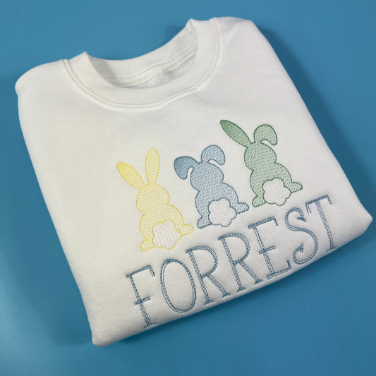 Folded white sweatshirt with embroidered bunnies and 'FORREST' on a blue background