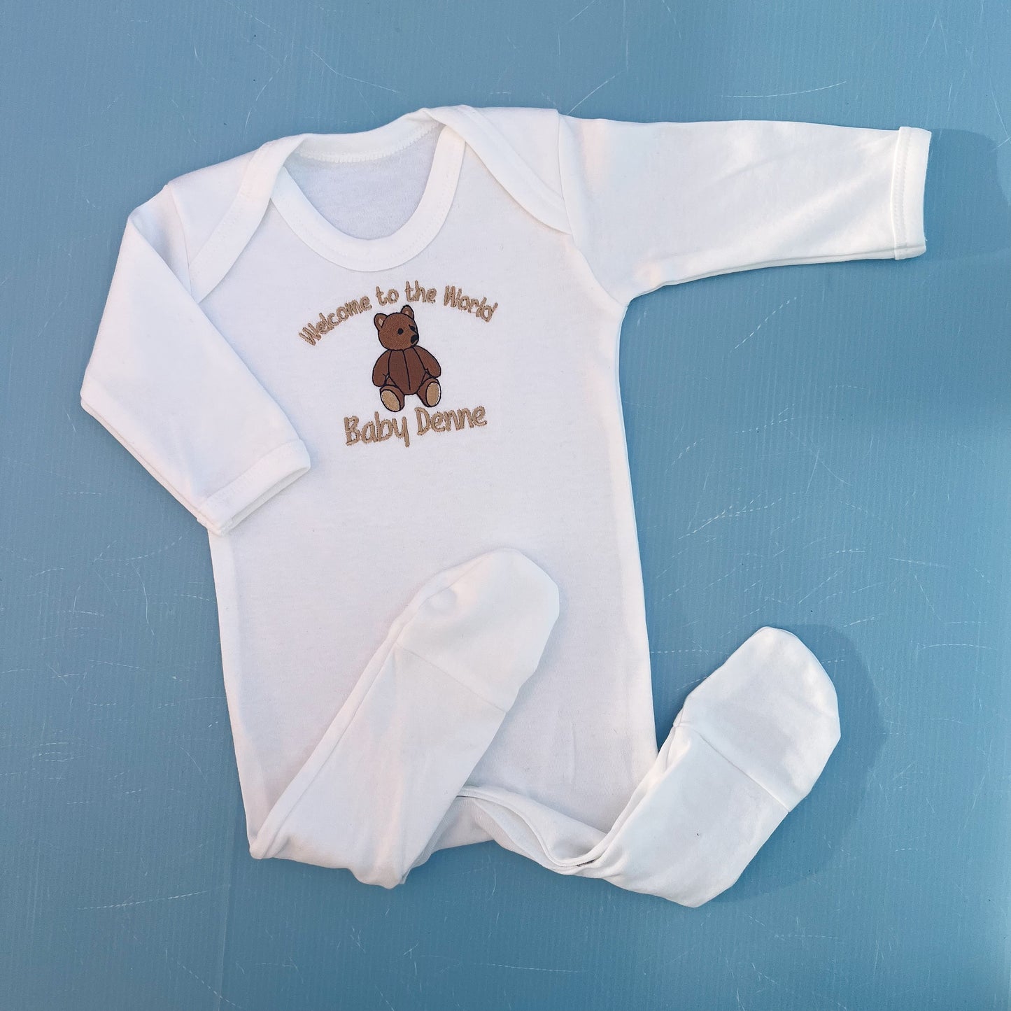 White baby onesie with teddy bear design and text on a blue background