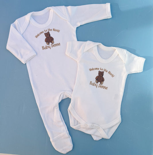 Two baby onesies with embroidered text and a bear design on a blue background