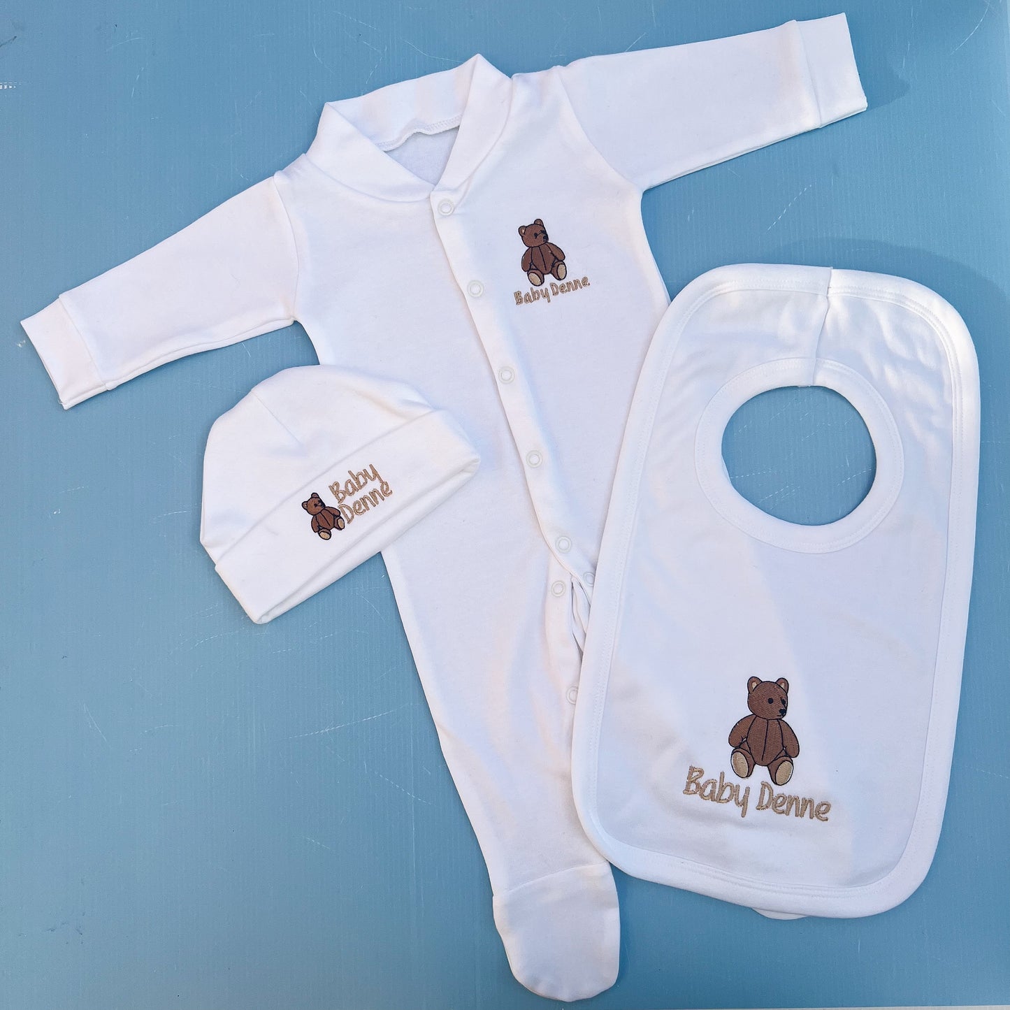 Baby clothing set with bib, hat, and onesie on a blue background