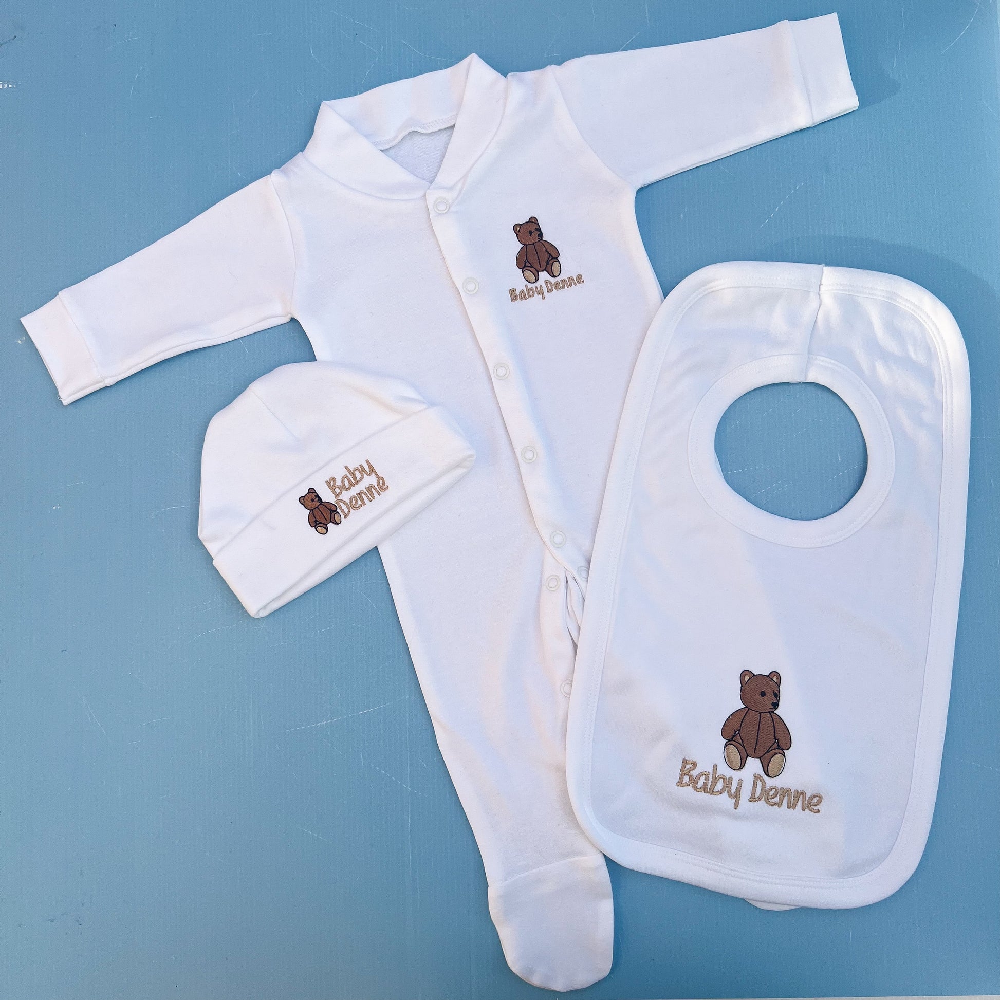 Baby clothing set with bib, hat, and onesie on a blue background