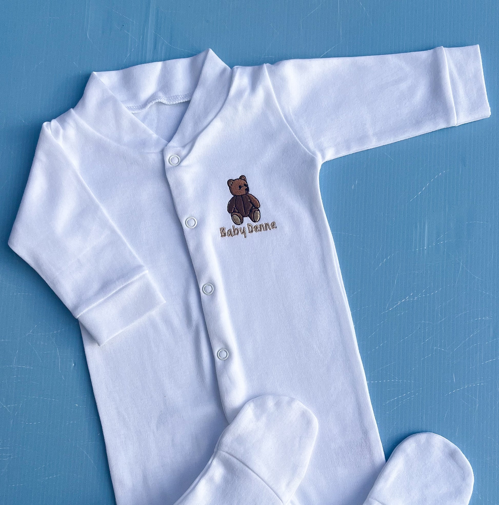 White Baby Sleepsuit with Traditional Bear with a teddy bear design and 'Baby Denne' text on a blue background