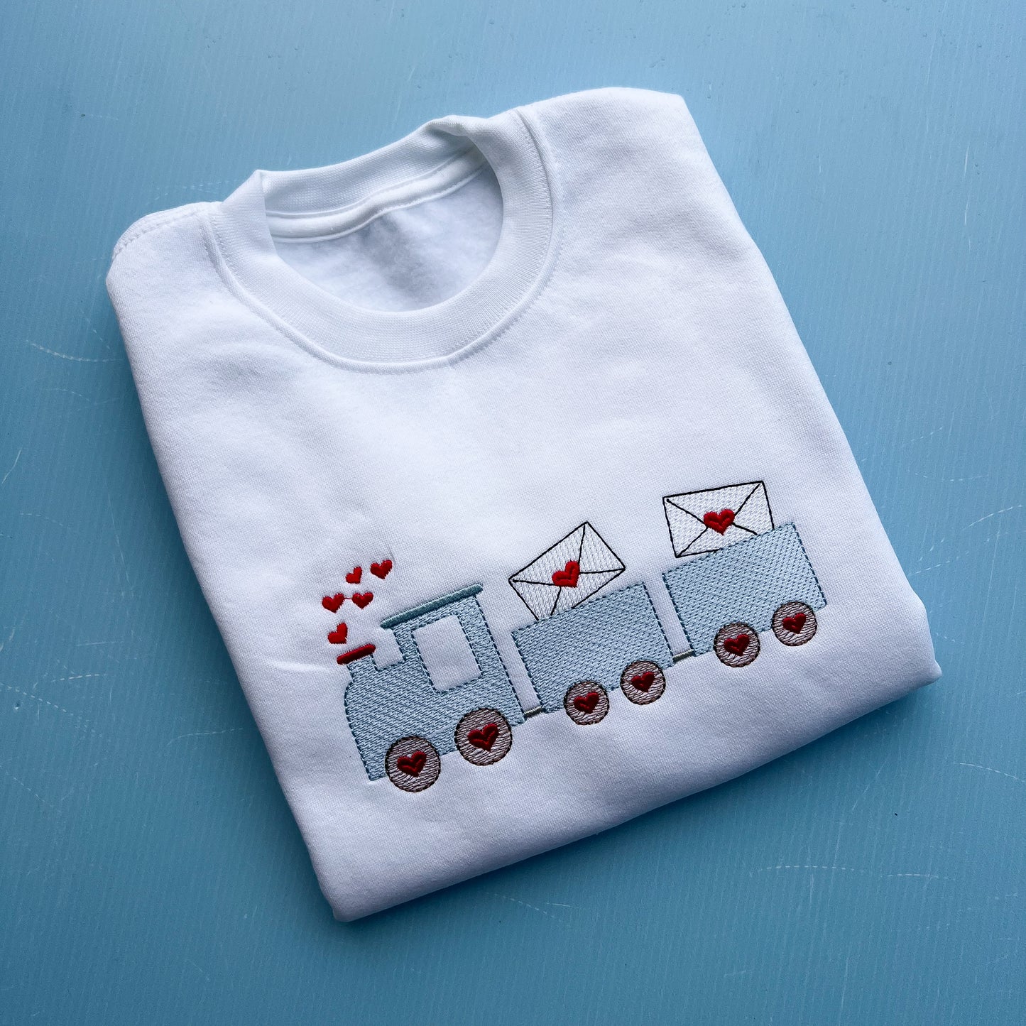Folded white sweatshirt with a blue train and heart designs on a blue background