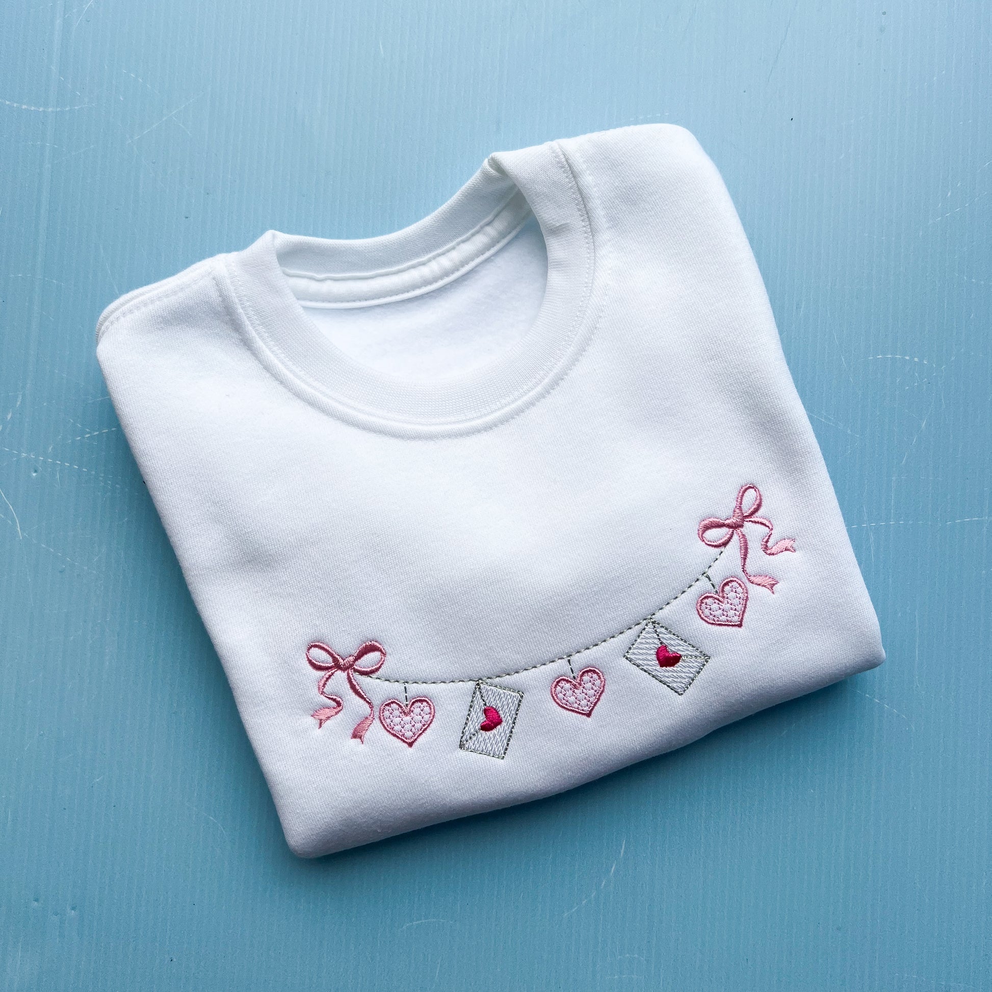 White jumper with a love letter chain with bows embroidered on the front