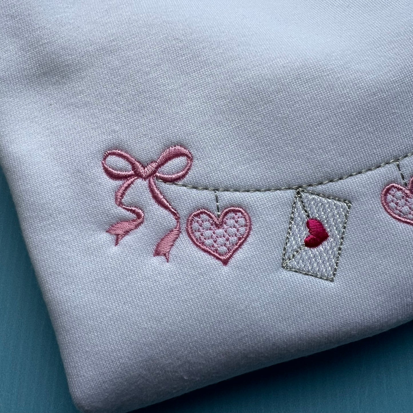 Embroidered heart and bow design on a light gray fabric background