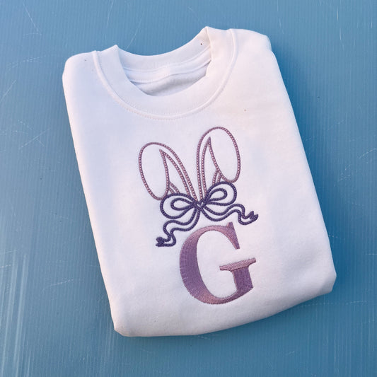 White jumper with embroidered bunny ears, a large bow and the letter G 