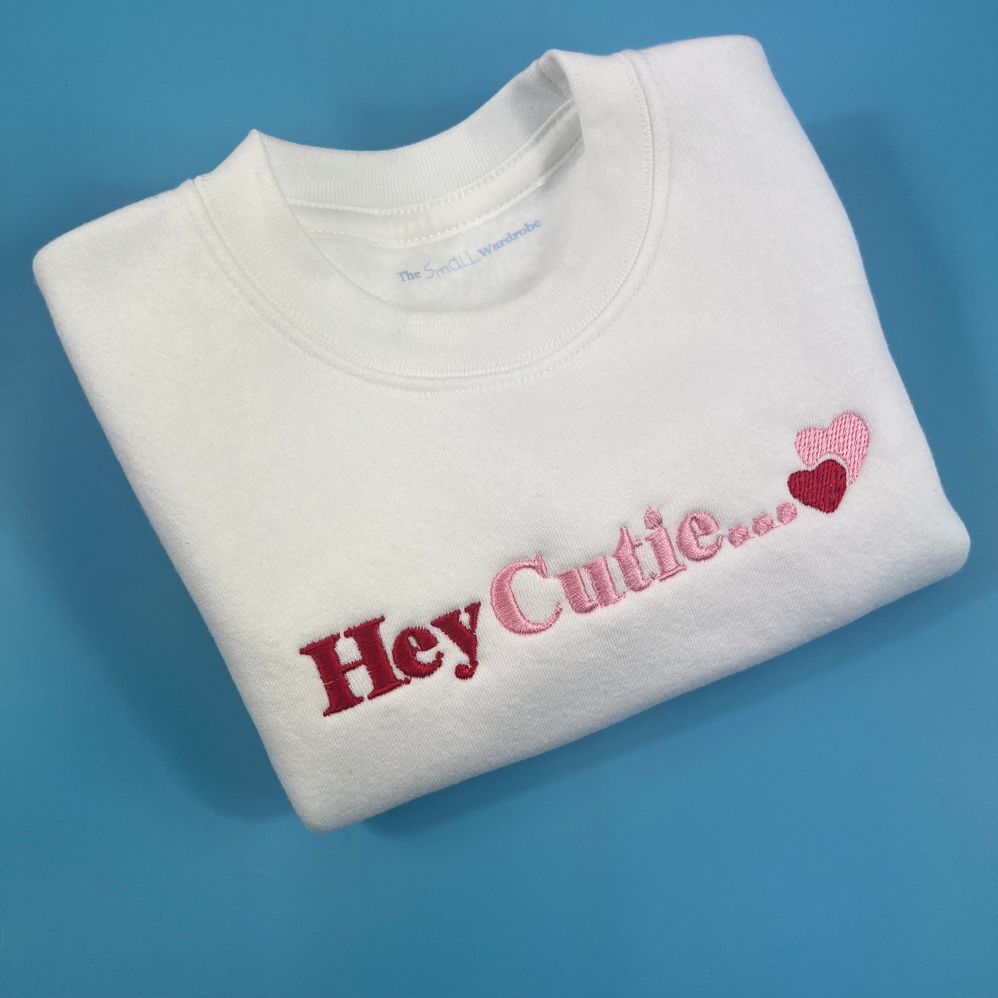 White sweatshirt with hey cutie embroidered on the front in pink and red 