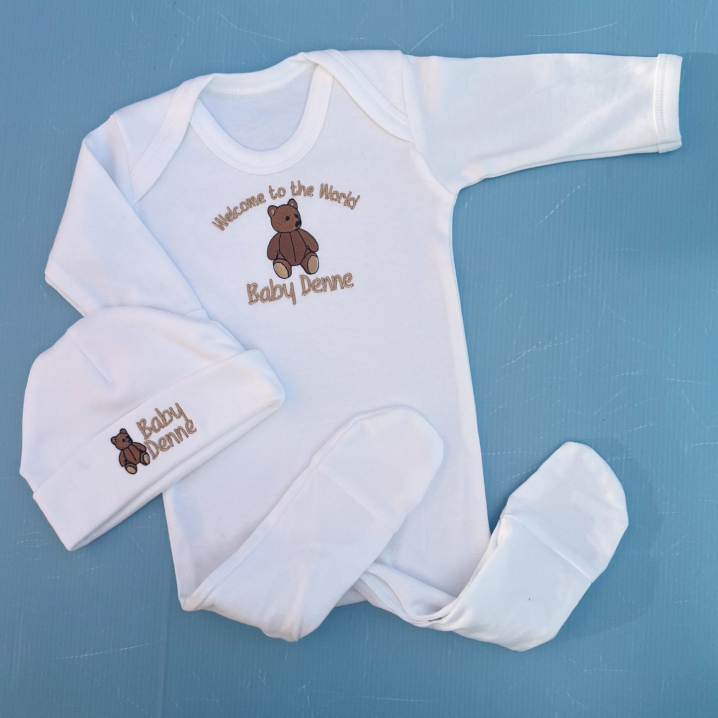 Baby clothing set with embroidered text and bear design on a blue background
