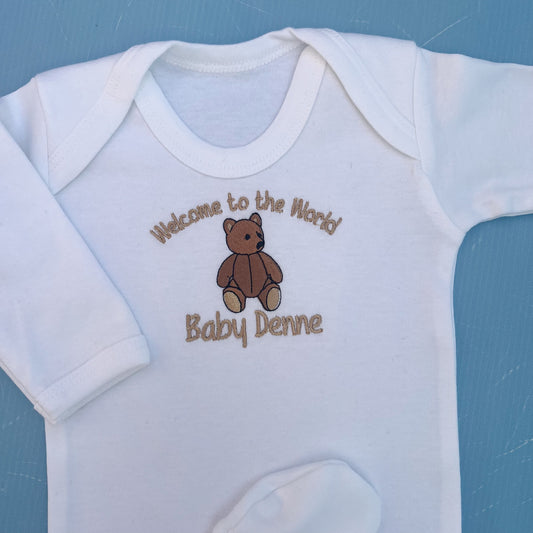 White baby onesie with brown teddy bear and text on a blue background
