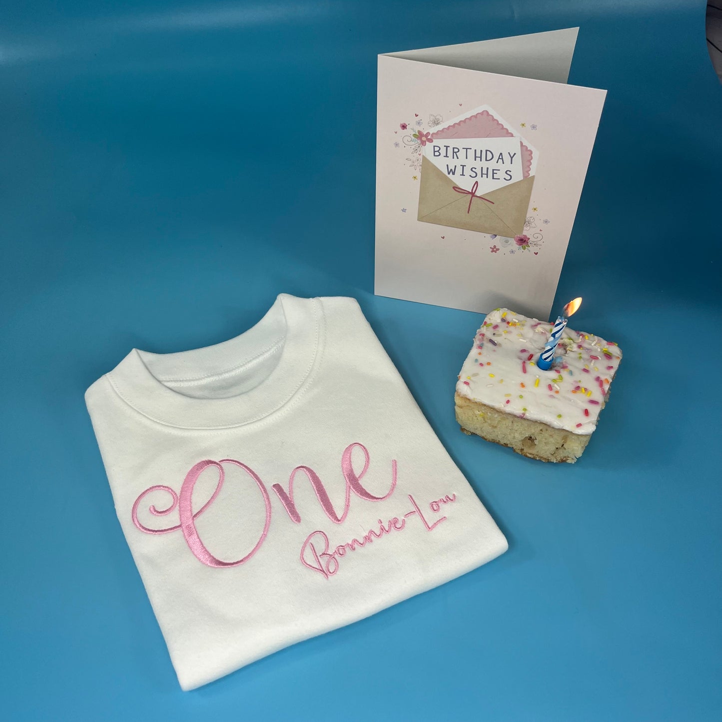 White t-shirt with 'One' and a birthday card on a blue surface