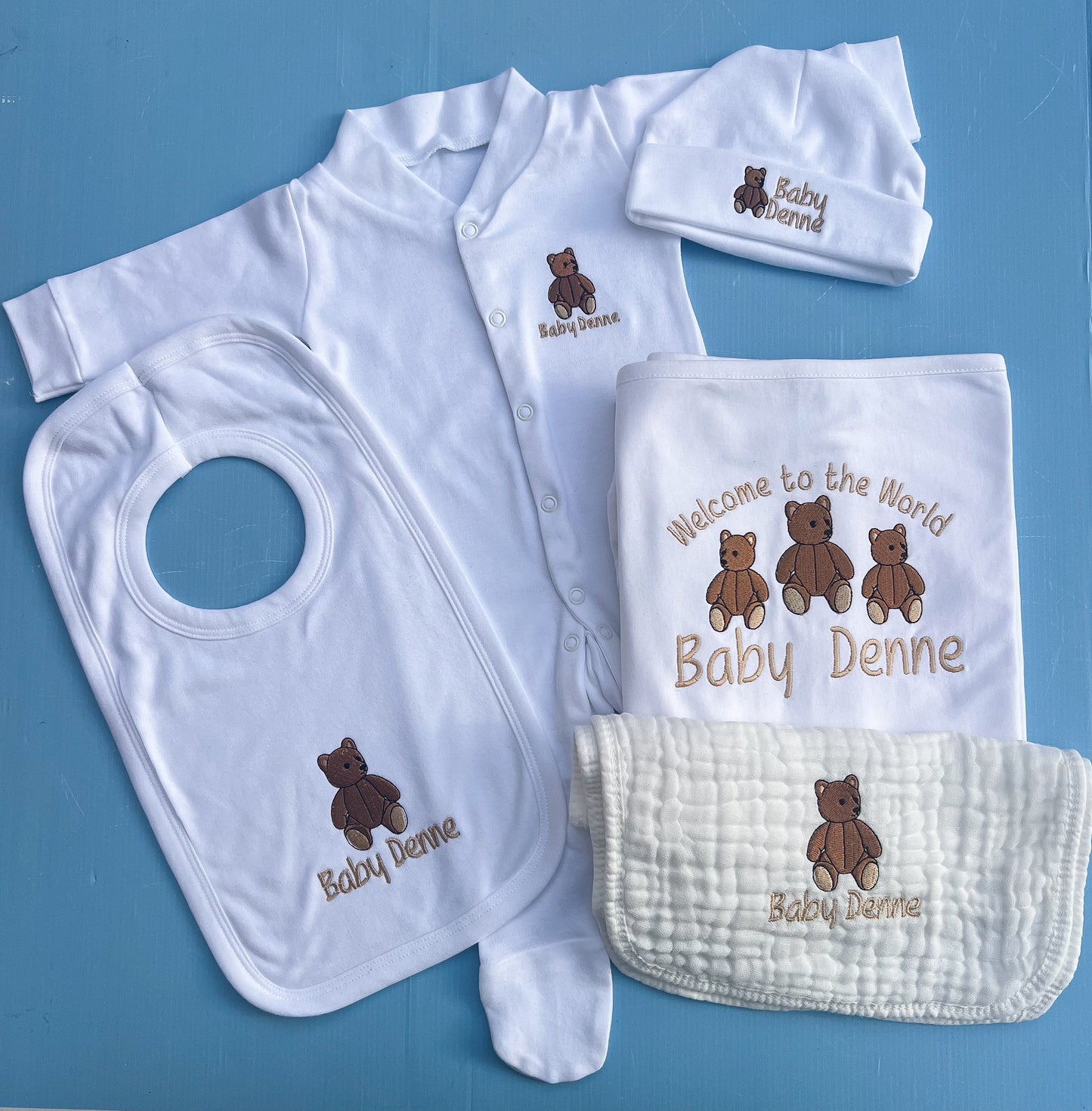 Baby clothing set with bib, onesie, hat, and blanket on a blue background