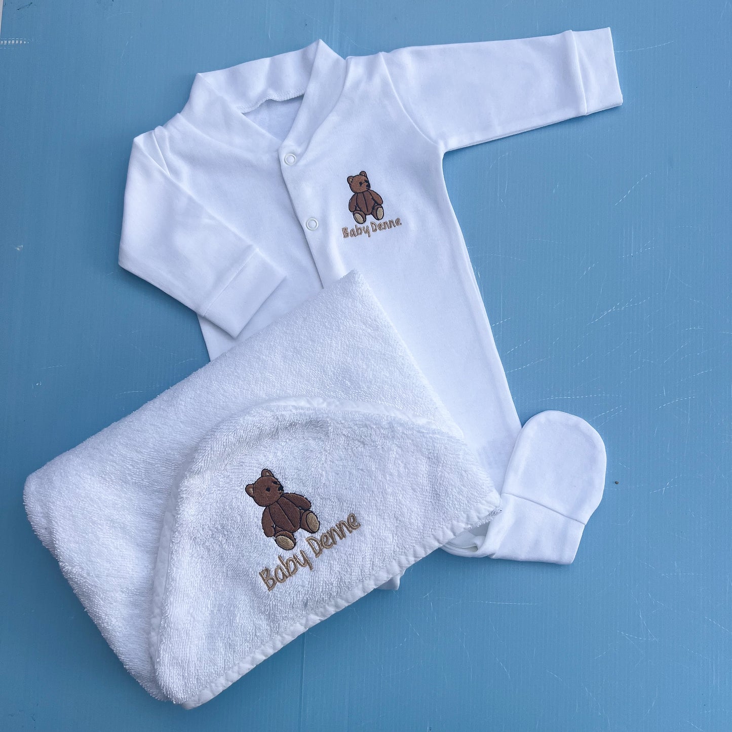 Baby clothing set with white babygrow and towel on a blue background