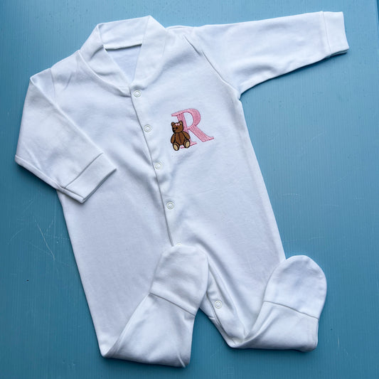 White baby onesie with a traditional teddy bear and letter 'R' on a blue background