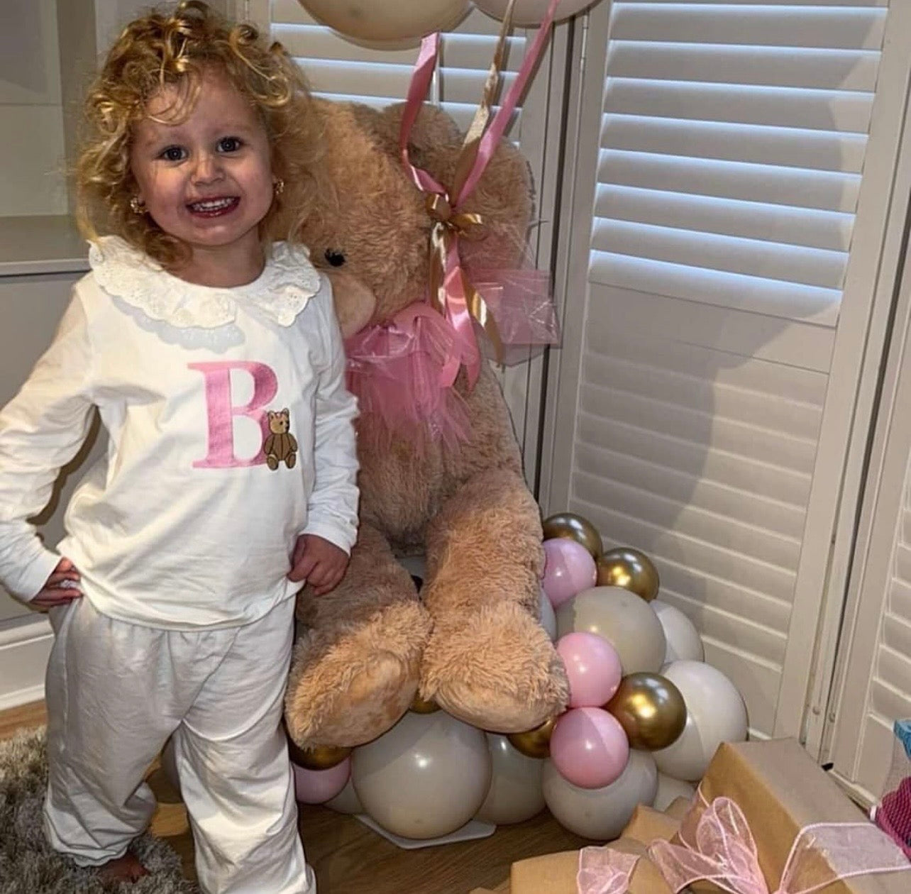 Child wearing White frill pyjamas with a big pink B with a traditional bear embroidered 