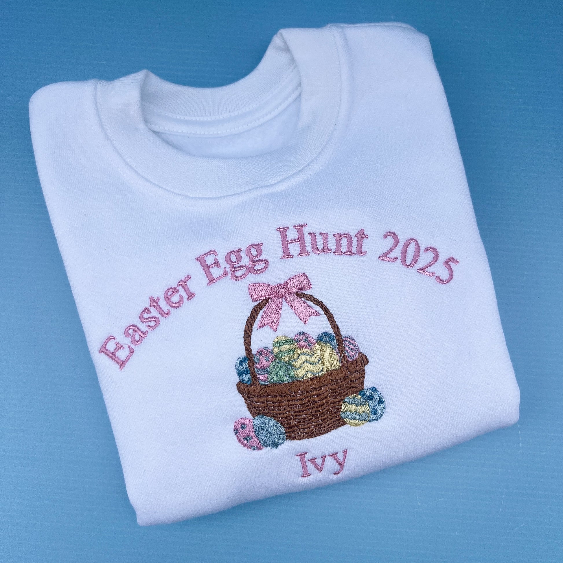 Folded white sweatshirt with Easter Egg Hunt 2025 design on a blue background
