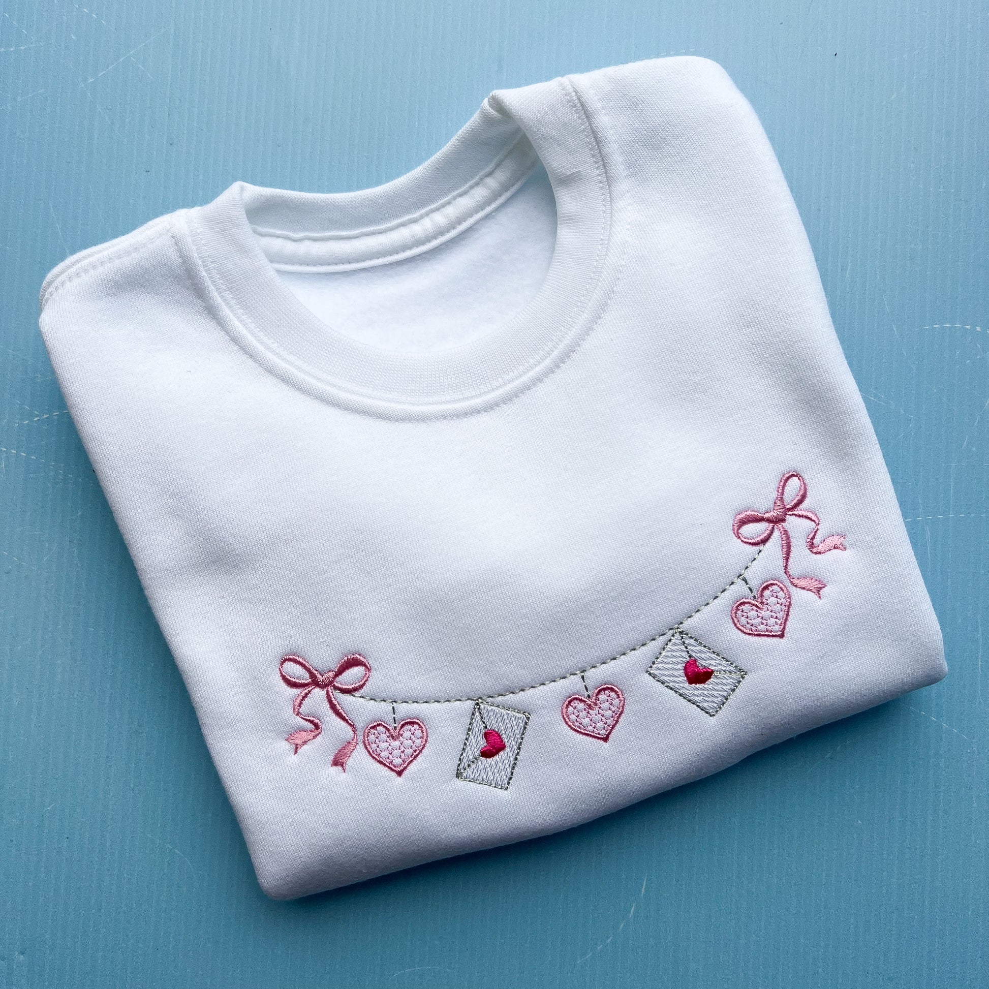 White jumper with a love letter chain with bows embroidered on the front