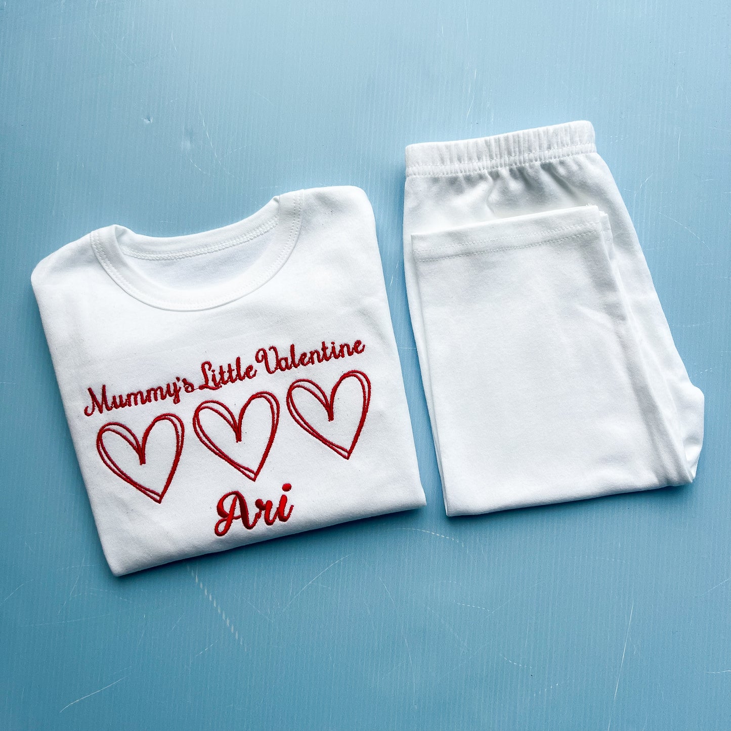 White t-shirt with red text and hearts and white pants on a blue background