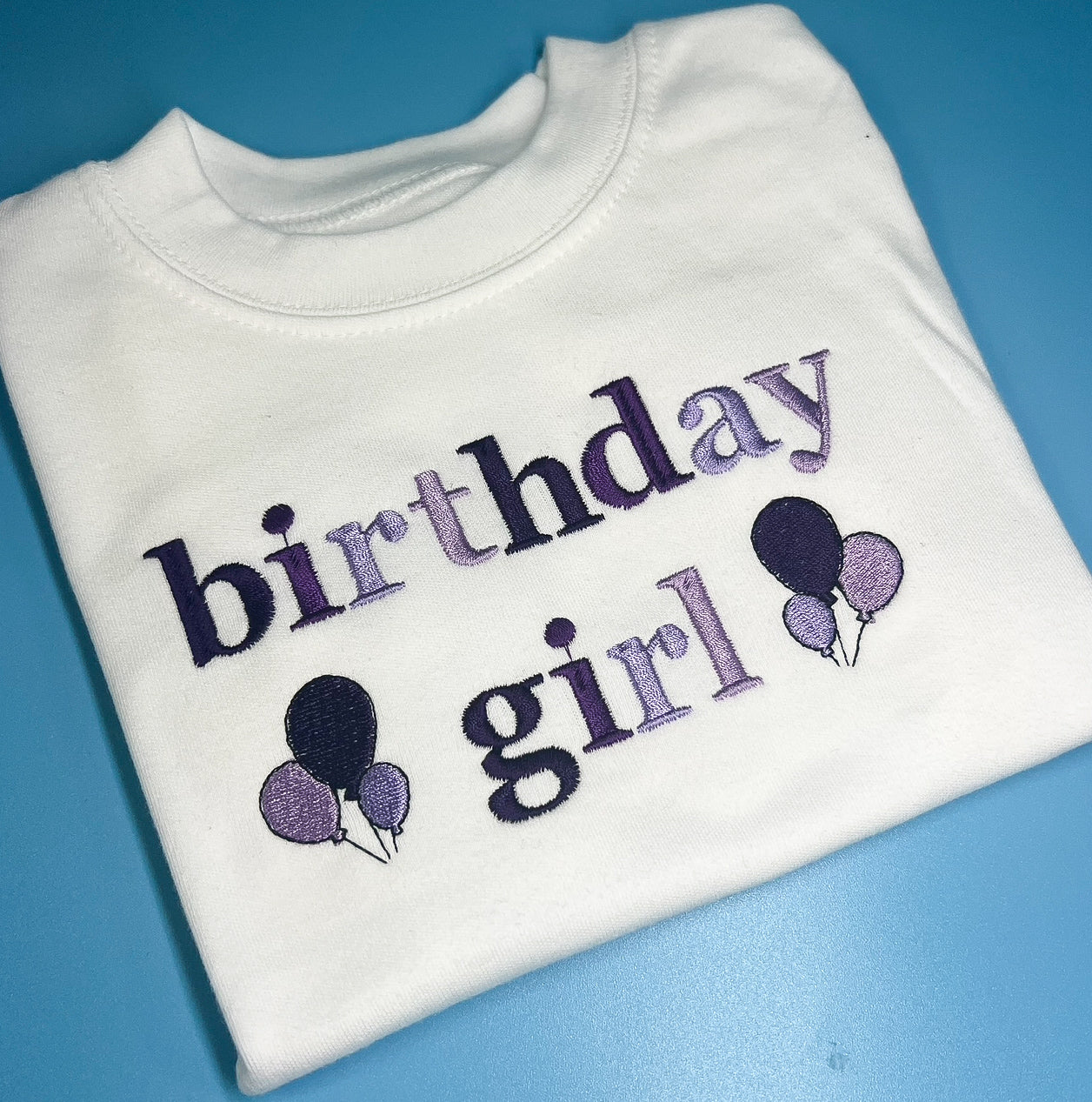 White sweatshirt with 'birthday girl' text and balloons on a blue background