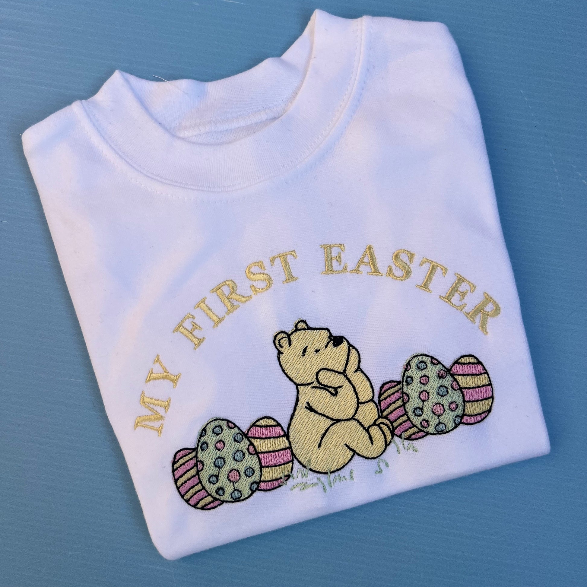 Folded white shirt with embroidered design of a bear and Easter eggs on a blue background