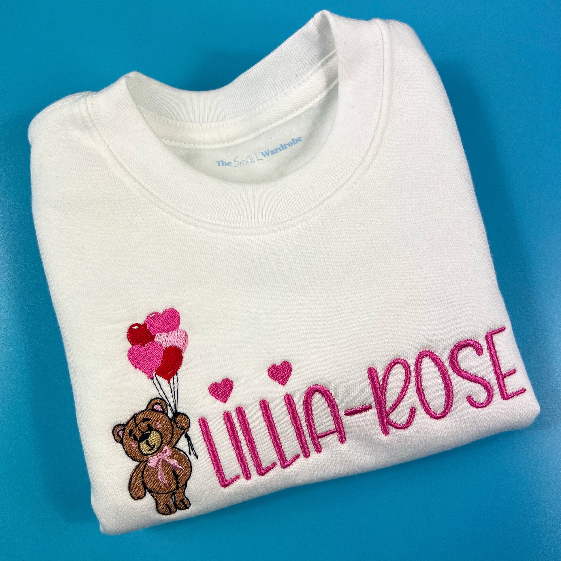 White sweatshirt with a bear holding heart balloons with child’s name embroidered on the front