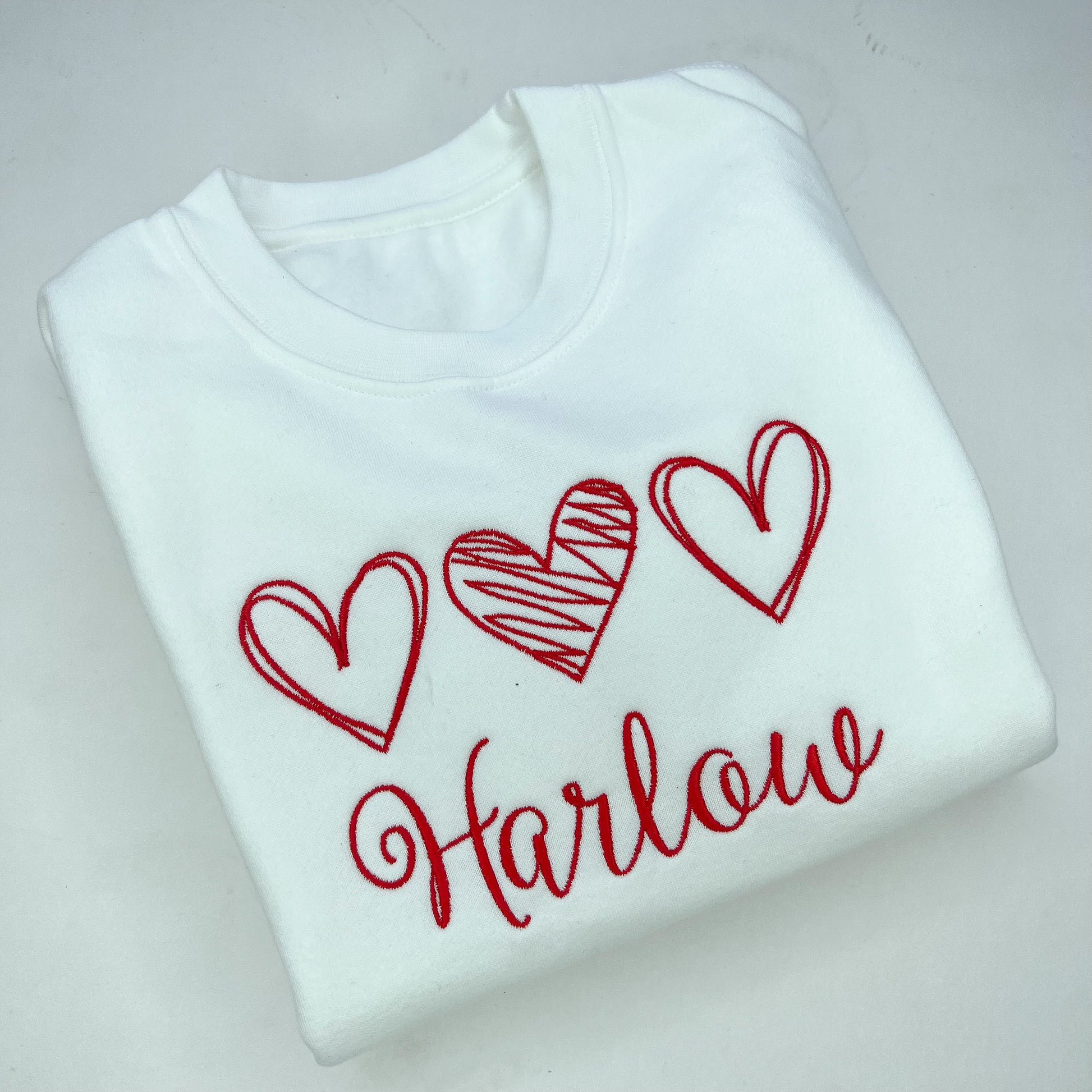 White sweatshirt with red hearts and 'Harlow' text on a light gray background