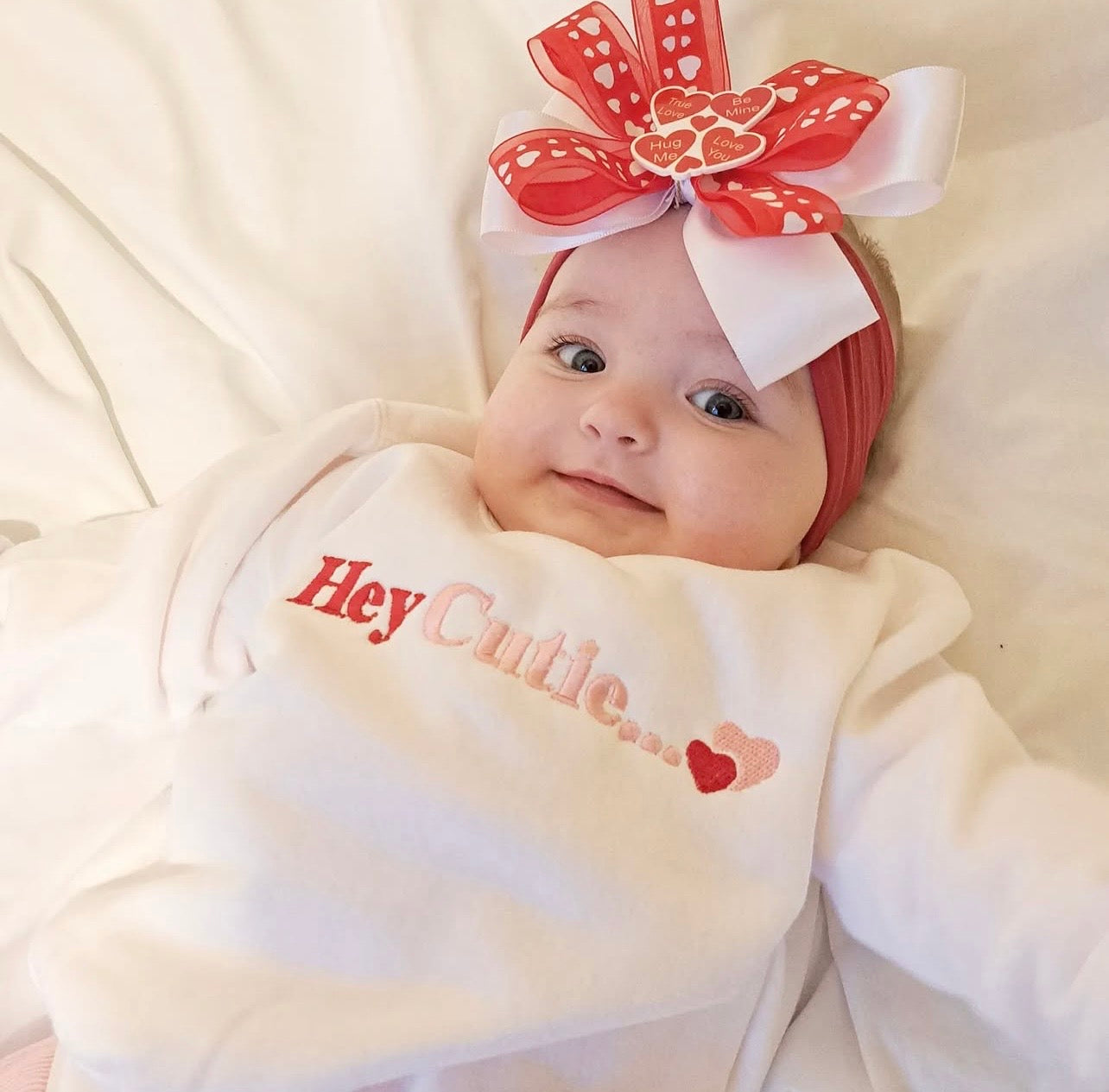 Baby girl wearing White sweatshirt with hey cutie embroidered on the front in pink and red 