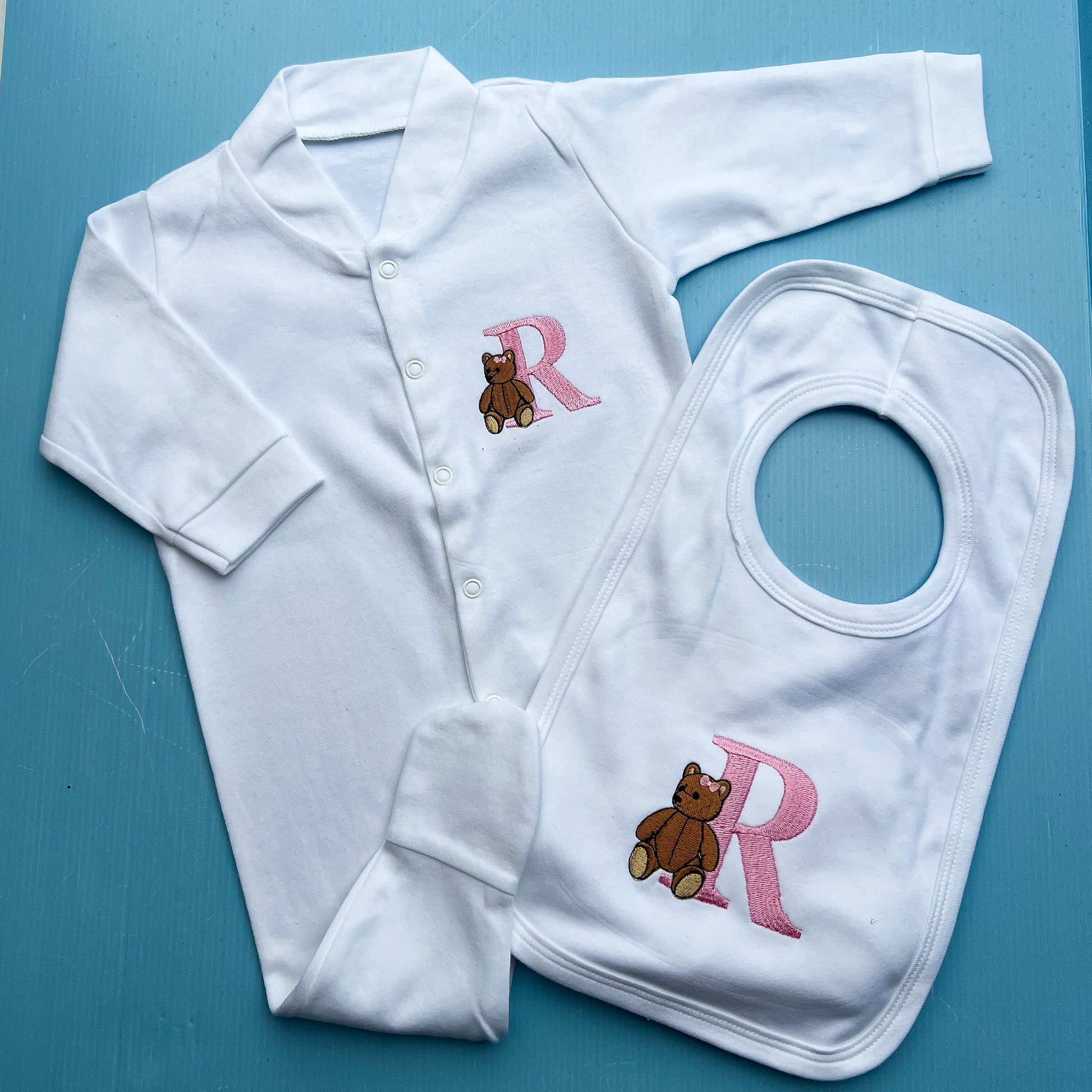 White baby outfit with teddy bear and 'R' design on a blue background