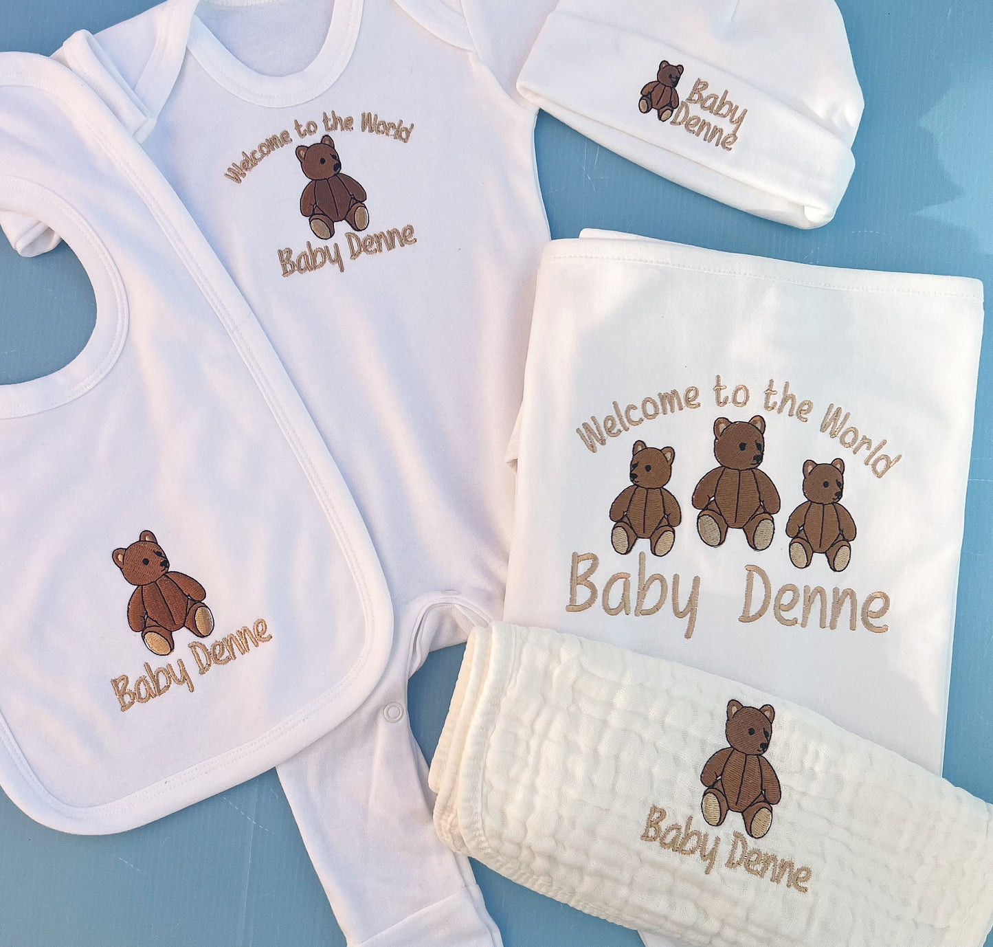 Baby clothing set with embroidered teddy bears and text on a blue background