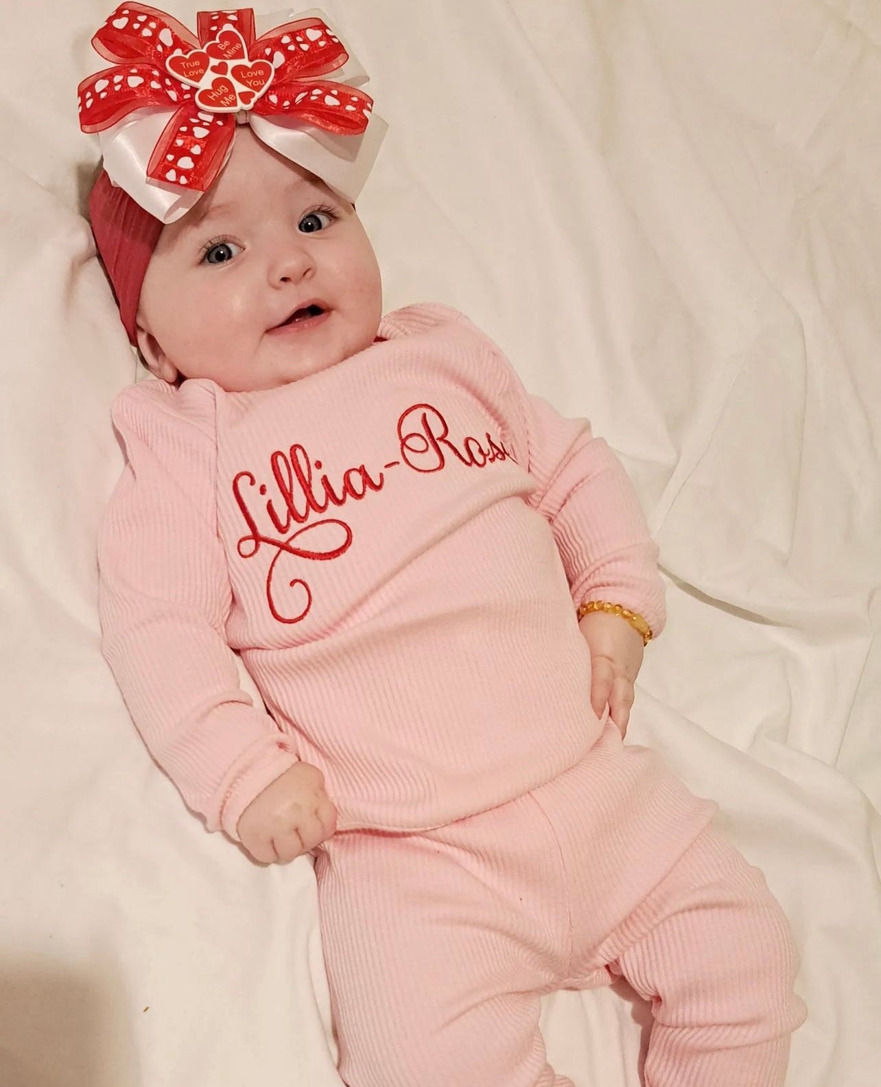Baby girl wearing pink ribbed tracksuit with lillia rose embroidered on the front in red 