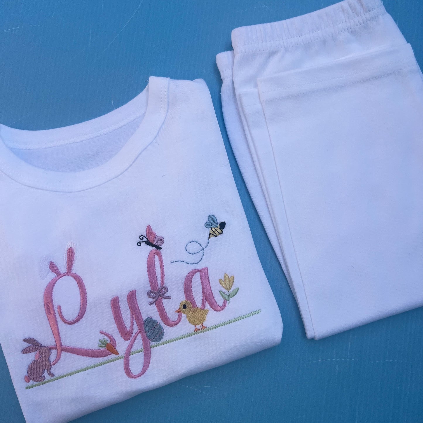 Name Lyla in pink with lots of Easter icons including, bunny rabbit ears, egg, bunny, chick, butter fly and bumble bee 