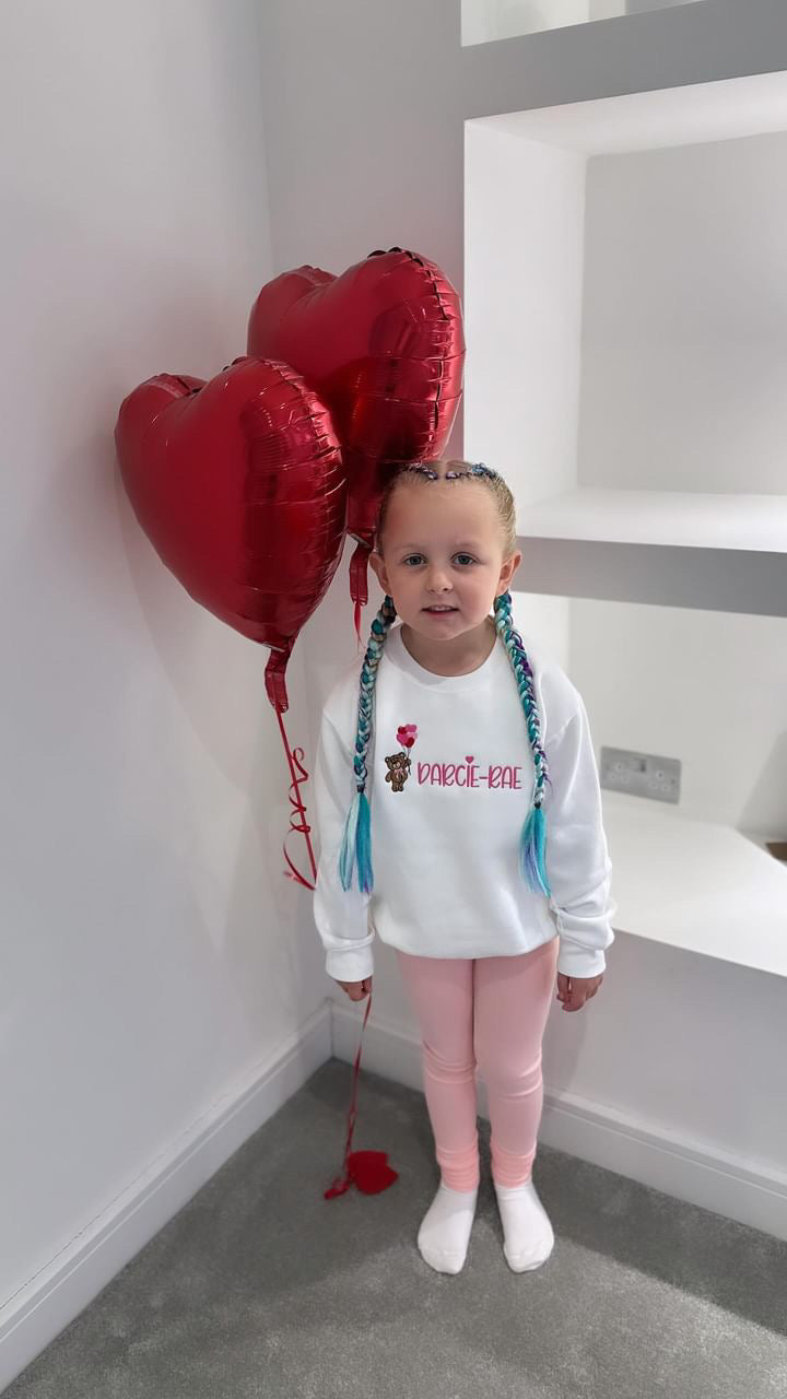Girl wearing White sweatshirt with a bear holding heart balloons with child’s name embroidered on the front