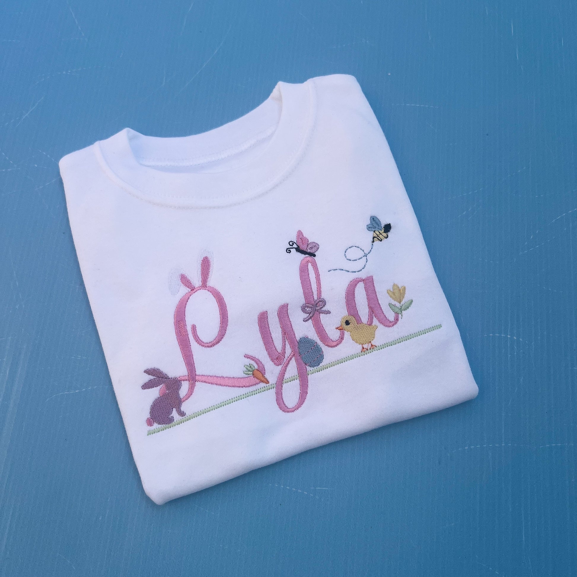 Name Lyla with lots of little Easter icons attached to it, Easter ears, bunny, carrot, bumble bee, flowers and chicks 