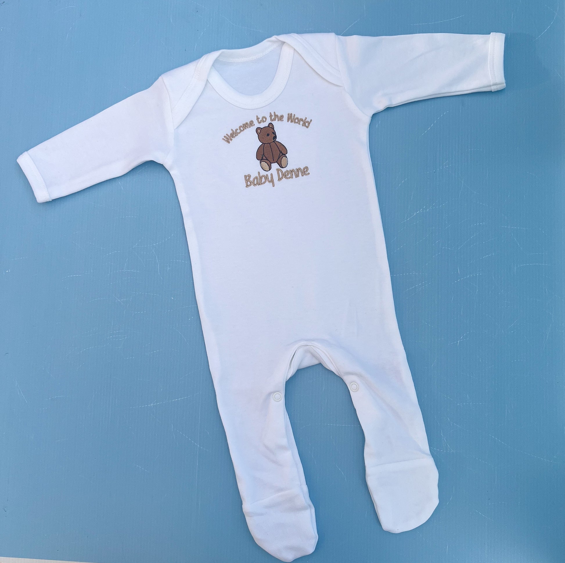 White baby onesie with teddy bear design and text on a blue background
